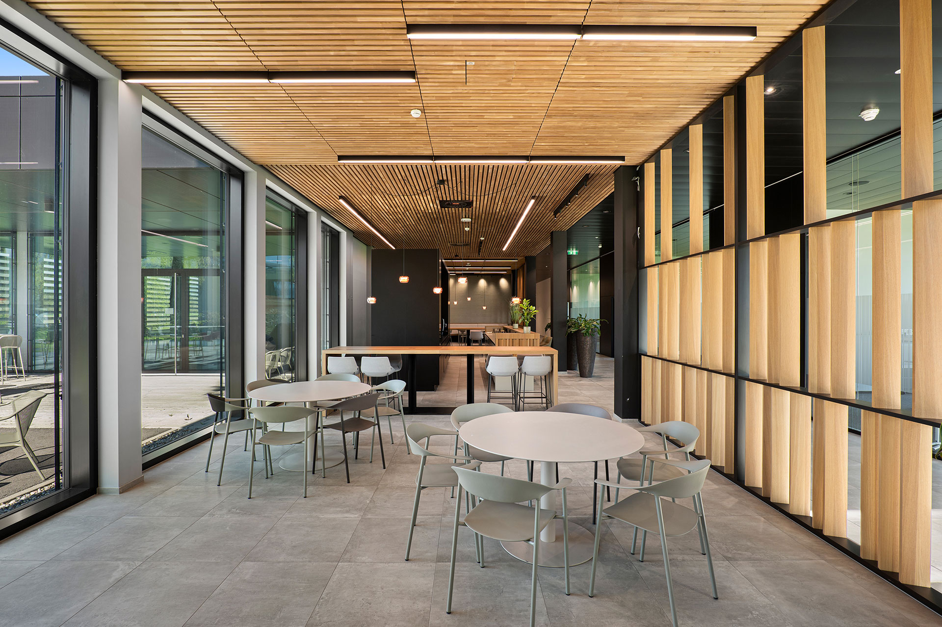 Das Bild zeigt die Cafeteria im Erdgeschoss der Bürokomplex Schlatt 1 in Hohenems. Der Aufenthaltsraum verfügt über mehrere Tische sowie Bartische und kann für Mittagspausen, Kaffeepausen und After-Work-Drinks genutzt werden.